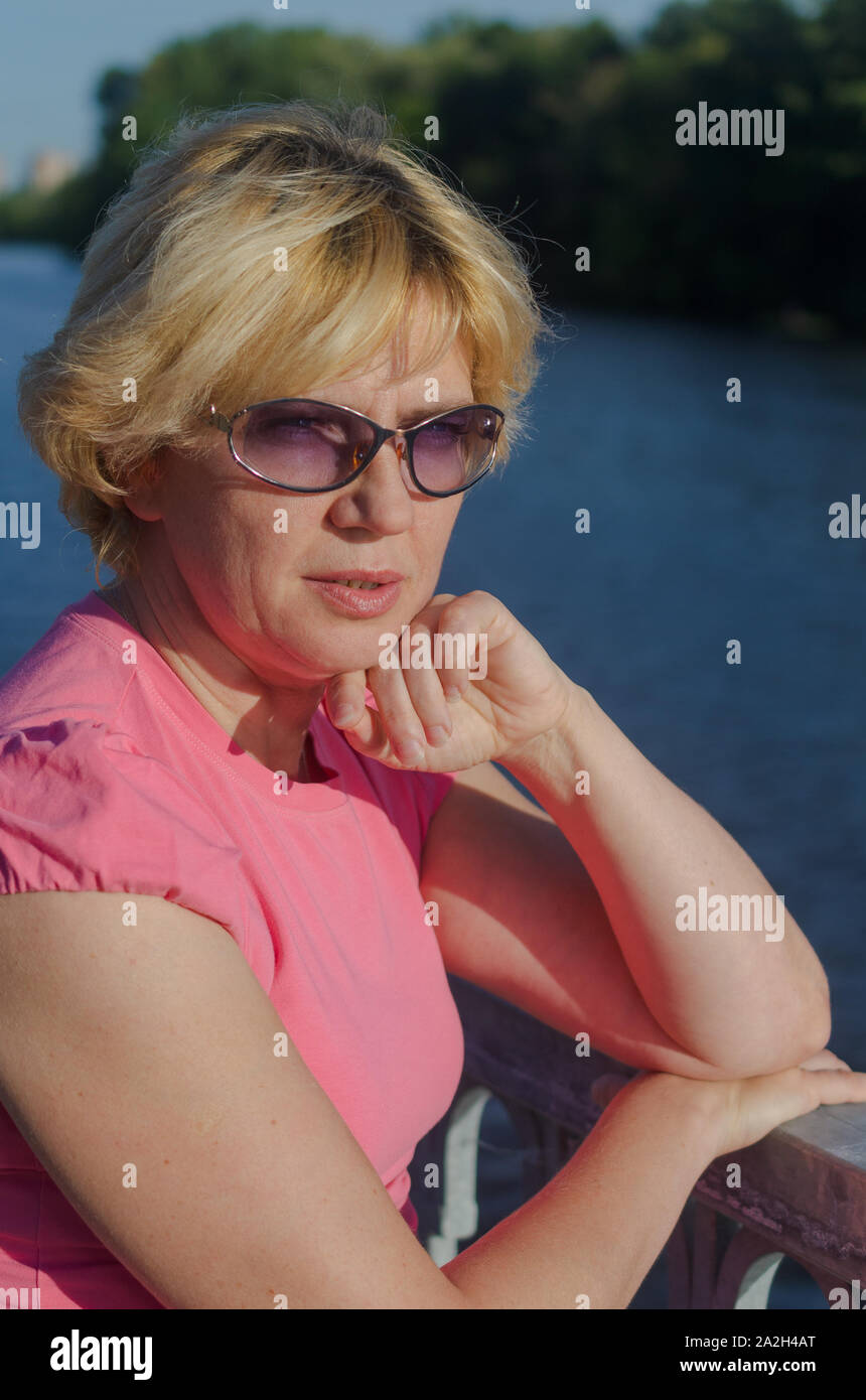 Eine Frau von 45-50 Jahre alt sitzt mit Traurigkeit in der Nähe des Flusses auf dem Damm Straße Stockfoto