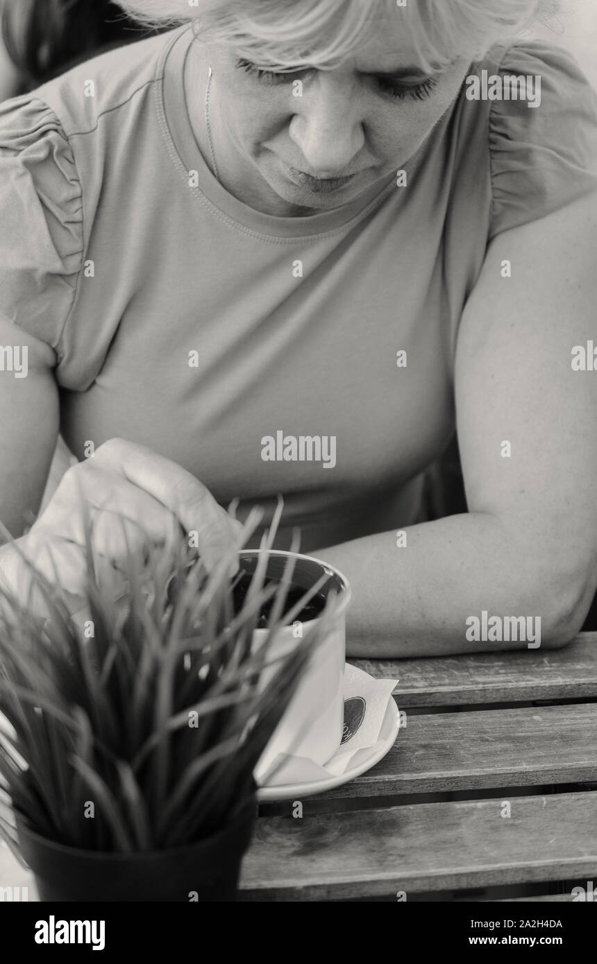 Eine Frau von 45-50 Jahre alt sitzt traurig in einem Café bei einer Tasse Kaffee Stockfoto