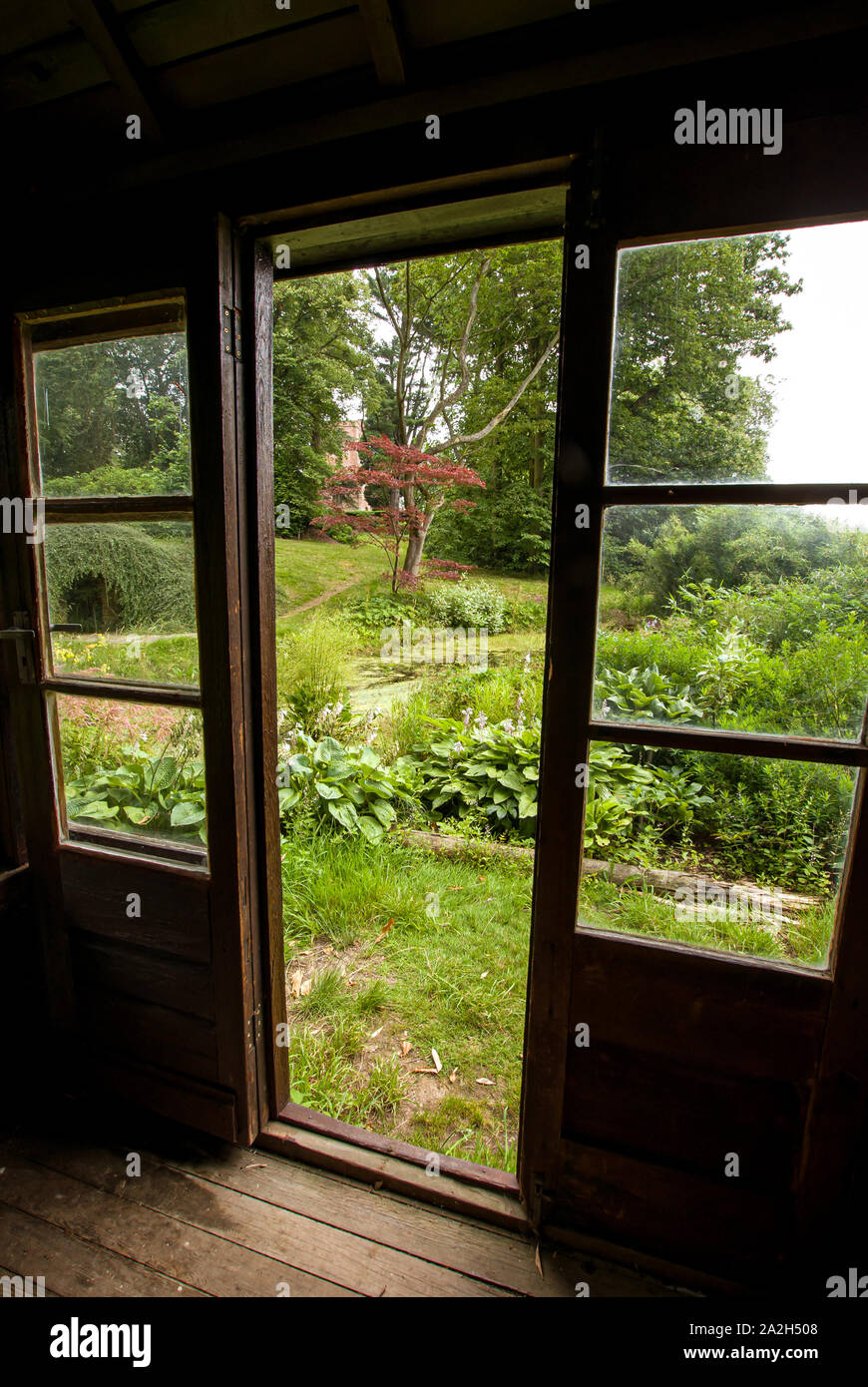 Blick auf einen üppigen Garten durch die Türen und Fenster aus Holz Gartenhaus Stockfoto