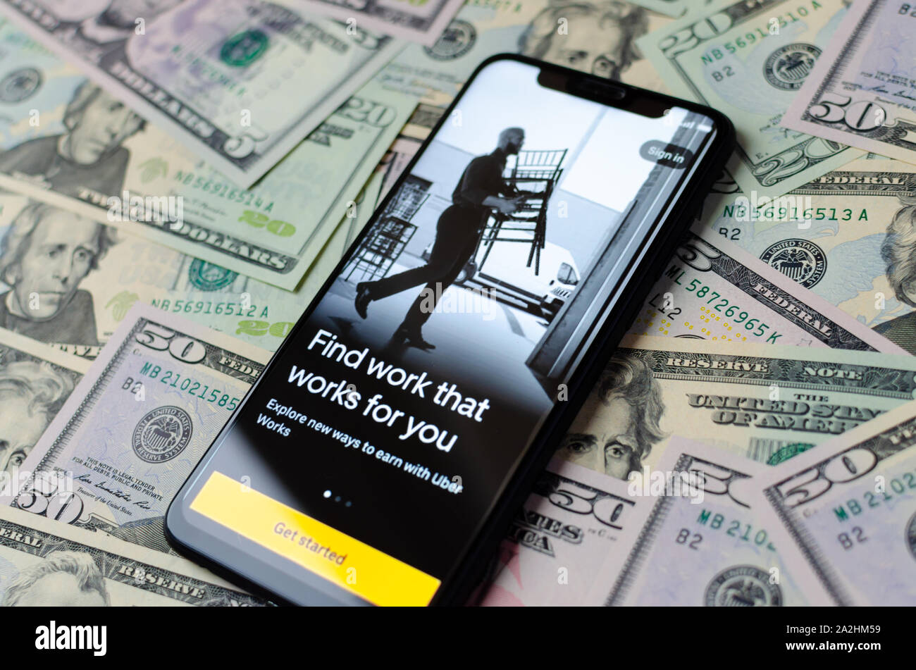 Uber Works App start Bildschirm auf dem Smartphone und Dollarscheine für den Hintergrund. Uber ein Arbeitsmarkt. Foto mit selektiven Fokus. Stockfoto