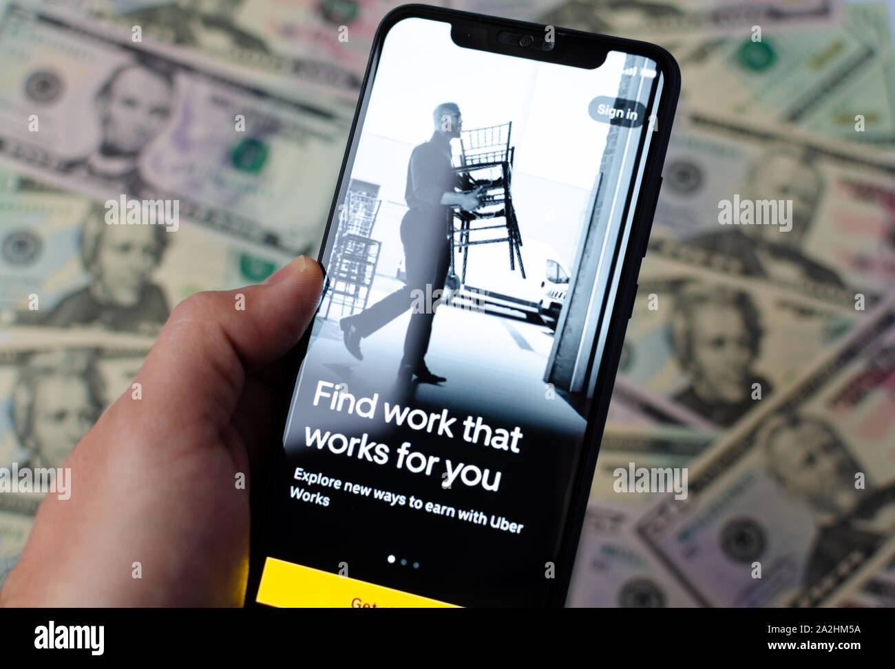 Uber Works App start Bildschirm auf dem Smartphone und Dollarscheine für den Hintergrund. Uber ein Arbeitsmarkt. Foto mit selektiven Fokus. Stockfoto