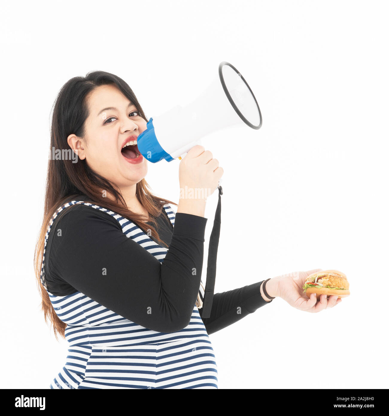 Eine junge fette Frau spricht mit einem Megaphon und es ist ein Hamburger in der Hand. Sie lächelt und glücklich, das Essen, das Sie essen mag. Sie ist hungrig. Uhr Stockfoto