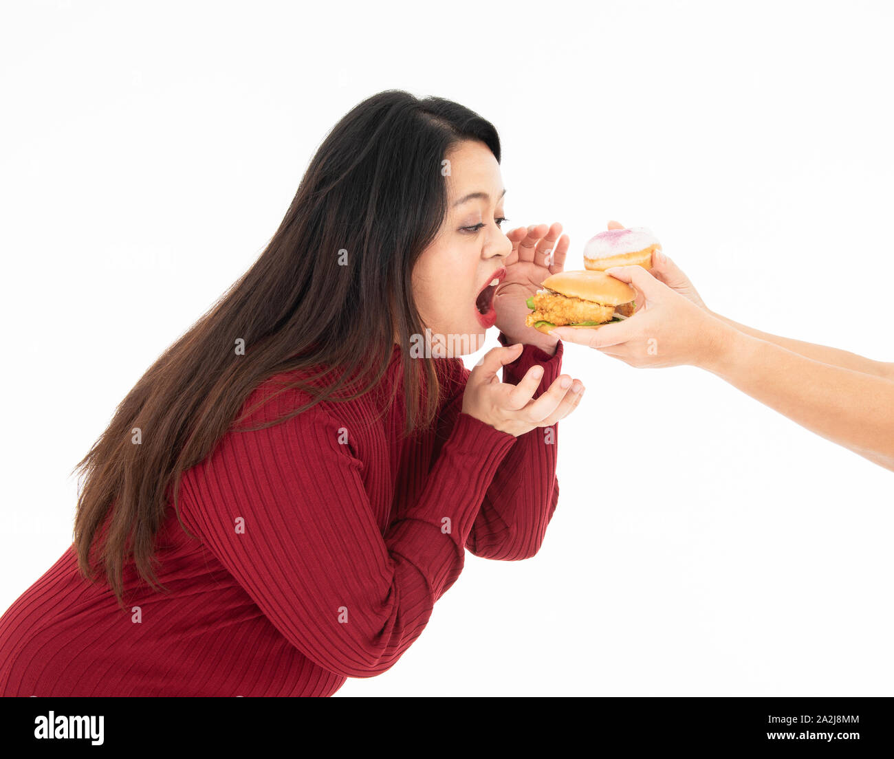 Eine junge fette Frau in Rot gekleidet war Essen einen Hamburger und Krapfen, die übergeben wurde. Sie ist hungrig und ihr Lieblingsessen. Gesundes Konzept. Stockfoto