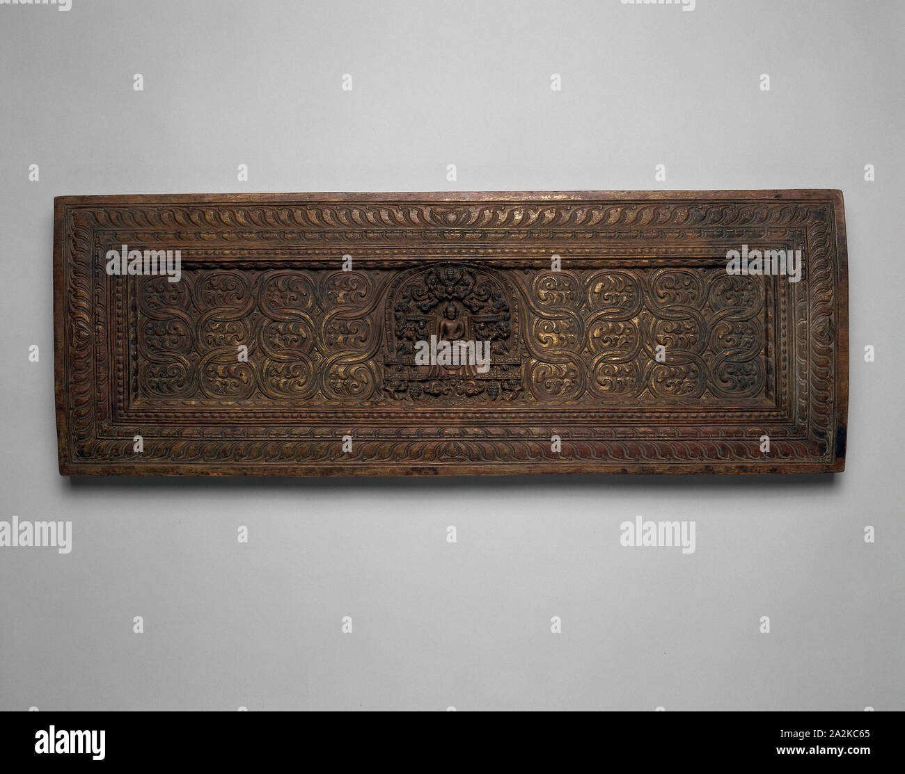 Manuskript Abdeckung mit verankert Sakyamuni Buddha mit Hand in die Erde berührt () Bhumisparsha Mudra, 15. Jahrhundert, Tibet, Tibet, Tibet, Holz mit Spuren von Vergoldung, 25,2 x 70,8 x 3,9 cm (9 15/16 x 27 7/8 x 1 1/2 in. Stockfoto