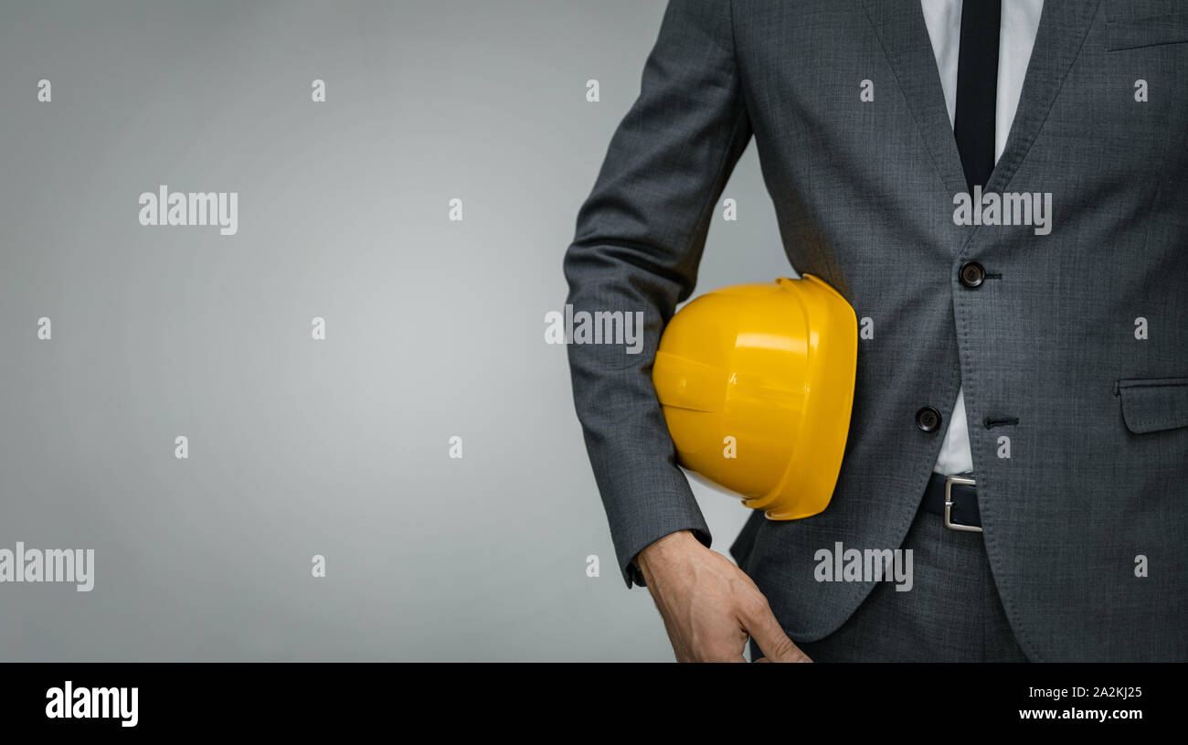 Bauindustrie Business - Geschäftsmann Holding gelben Schutzhelm Unterarm auf grauem Hintergrund mit Kopie Raum Stockfoto