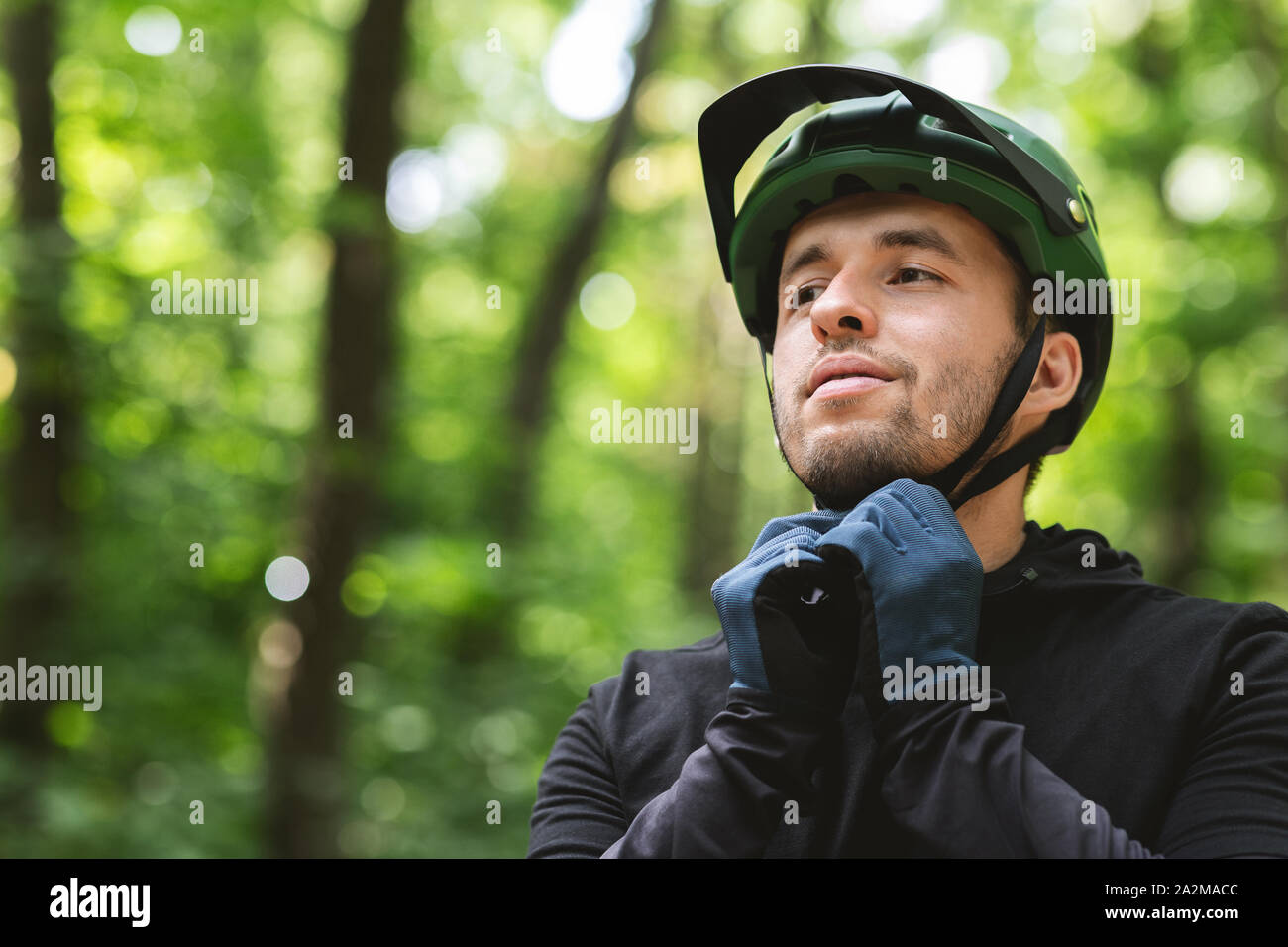 Junger Mann seinen Sport Helm auf Wald Hintergrund tragen Stockfoto