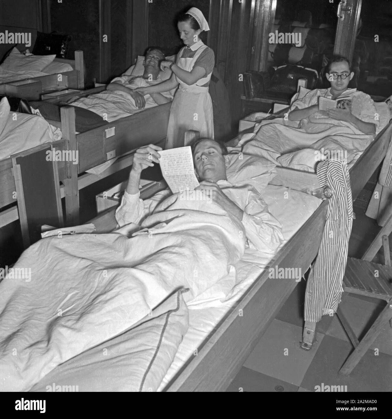 Original-Bildunterschrift: LAZARETTSCHIFF "Wilhelm Gustloff"-Der Rauchsalon des KdF-Schiffes wurde in einen Schlafsaal und Verwundeten umgewandelt; eine Rot Kreuz Schwester bei einem Soldaten. Krankenhaus Schiff "Wilhelm Gustloff" - den Raucherzimmern in einem Schlafsaal für die verwundeten Soldaten geändert wurden; ein Rotes Kreuz Krankenschwester helfen, ein Soldat. Stockfoto