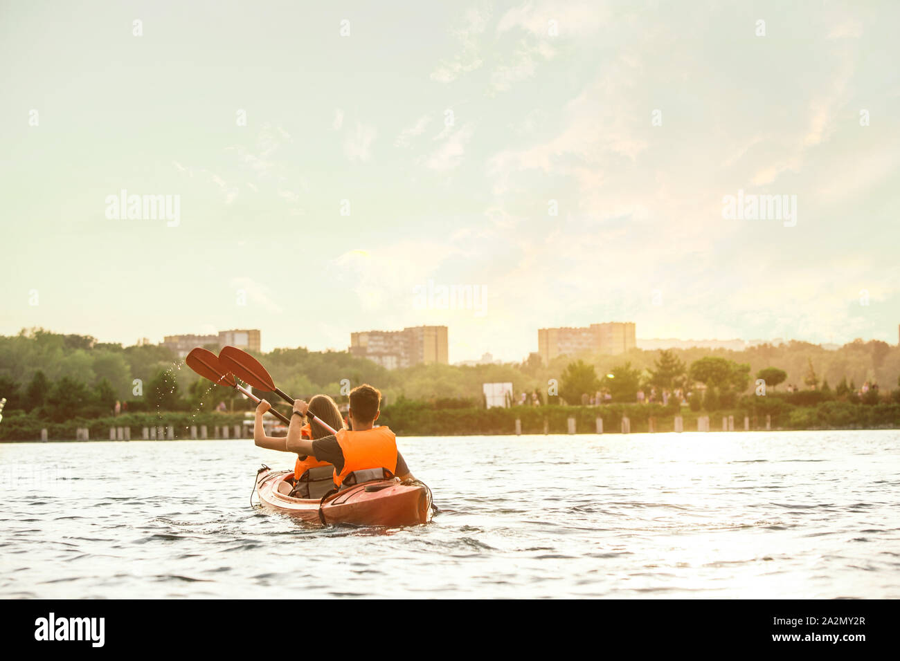 Glückliche Junge kaukasier Paar Kajakfahren auf dem Fluss mit Sonnenuntergang im Hintergrund. Spaß in der Freizeit. Gerne männliche und weibliche Modell laughting auf dem Kajak. Sport, Beziehungen Konzept. Farbenfroh. Stockfoto