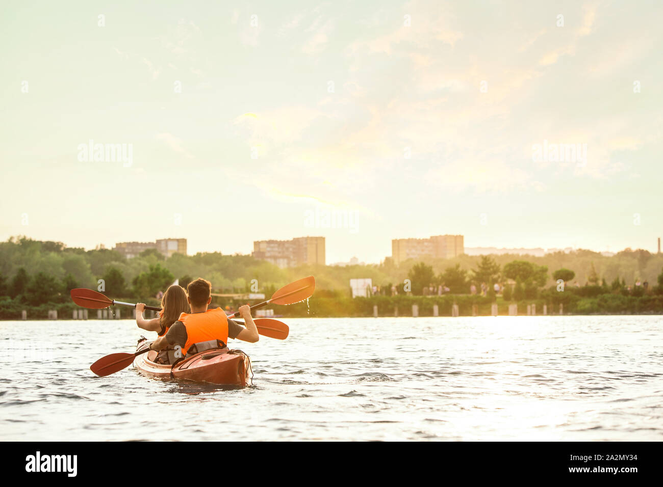 Glückliche Junge kaukasier Paar Kajakfahren auf dem Fluss mit Sonnenuntergang im Hintergrund. Spaß in der Freizeit. Gerne männliche und weibliche Modell laughting auf dem Kajak. Sport, Beziehungen Konzept. Farbenfroh. Stockfoto