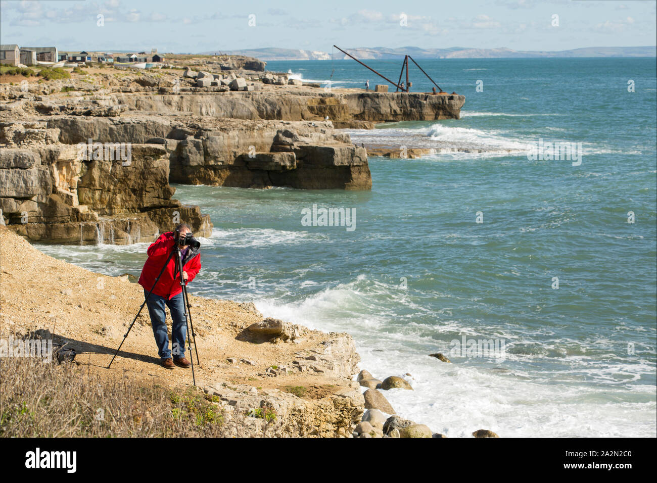 Ein Fotograf an einem windigen Tag fotografieren mit einem Stativ auf den Klippen von Portland Bill, Isle of Portland England UK GB Stockfoto