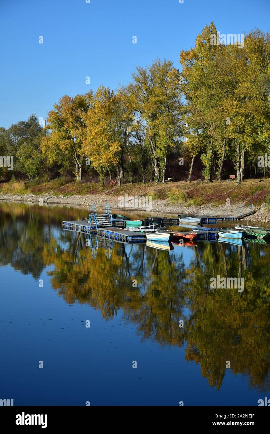 Herbst Landschaft. Ein See, ein Boot Brücke und einige Boote mit gelben und grünen Bäumen im Hintergrund. 68782 Bruehl, Baden-Württemberg, Deutschland. Stockfoto