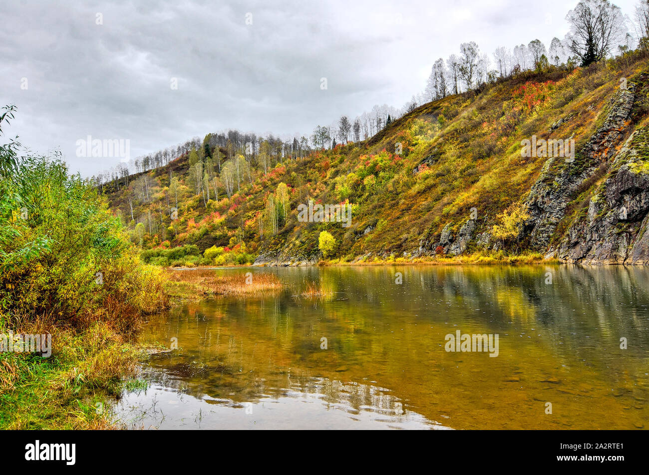 Herbst Landschaft auf dem steinigen steilen Ufer des Berg River. Klippen mit hellen bunten Bäumen, Büschen und Gras bedeckt. Schönheit der Natur fallen Stockfoto