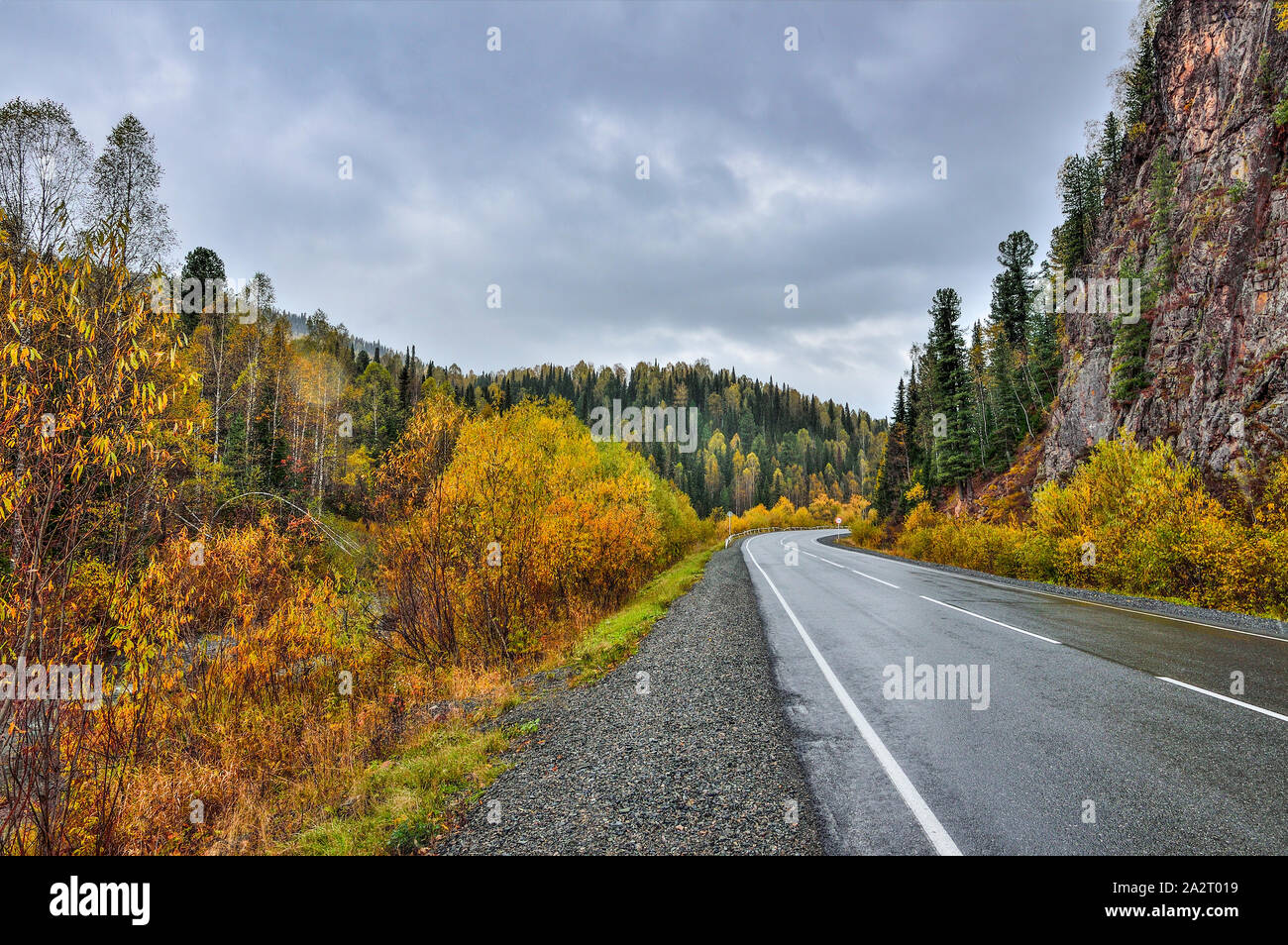 Herbst Landschaft - Schalten eines Berges Straße unter einer felsigen Klippe inmitten einer bunten Herbst Wald über die Berge. Golden Stockfoto