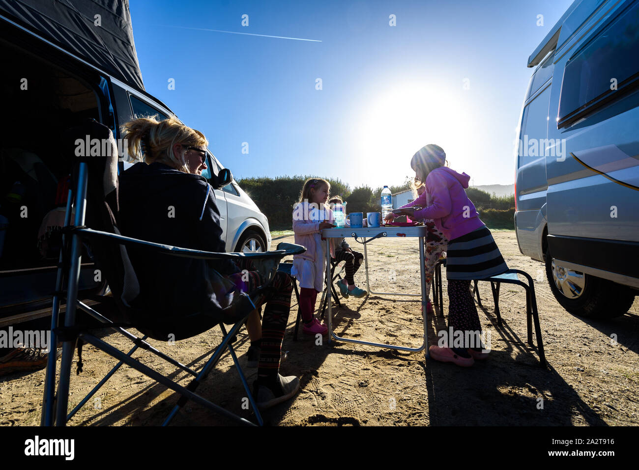 Reisemobil RV oder Wohnmobil auf einem Strand geparkt. Familie im Urlaub sitzt Außenseiten auf Camping Stühle und Tisch essen Frühstück, tolle Aussicht Stockfoto