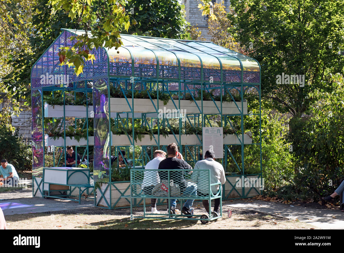 Drei Männer auf einer Bank von hinten mit Gewächshaus vor Smithfield Rotunde Garten West Smithfield, City of London, England Großbritannien UK Stockfoto