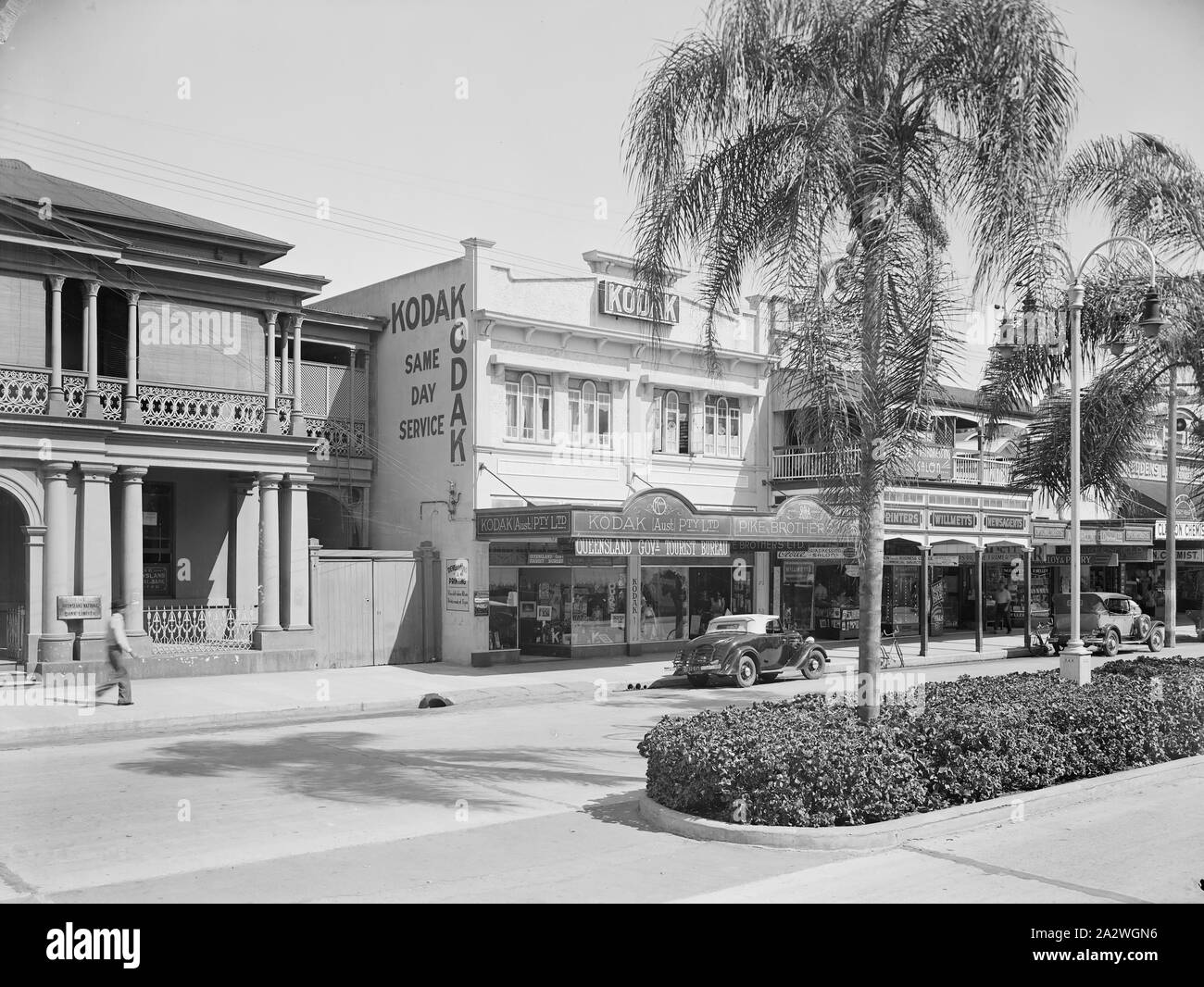Negative, Shop Exterieur Kodak Niederlassung, Townsville, QLD, 1930er Jahre, Schwarz-weiß Film negativ der Kodak Australasia Pty Ltd Filiale und die Bearbeitung am selben Tag Labor an der Flinders St, Townsville, Queensland, in den 1930er Jahren. Diese street view zeigt die benachbarten Geschäfte, eine begrünte Verkehrsinsel, und Autos und Fahrräder auf der Straße vor dem Hotel geparkt. Ein Mann geht aus der Vorderseite des Queensland National Bank auf der linken Seite des Schusses. Diese Kodak Shop war Stockfoto