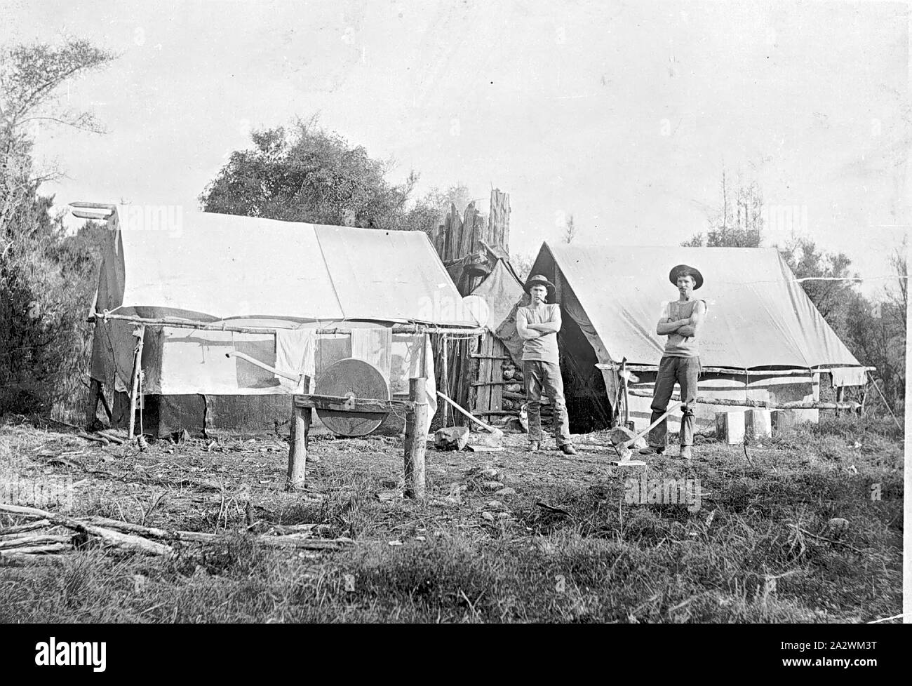 Negative - Holzfäller' Camp, Ballarat Bezirk (?), Victoria, ca. 1885, zwei Männer vor der Zelte ein Zelt hat einen Kamin aus Baumstämmen gebaut. Die Männer tragen Unterhemden, Hut und Hose, Es gibt zwei Achsen vor Ihnen. Es ist ein Schleifstein zum Schärfen der Achsen vor den Zelten, und es gibt viele Bäume im Hintergrund Stockfoto