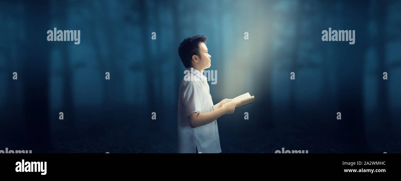 Junge Schule Junge in Uniform hält ein Buch in der dunklen kalten Wald in der Nacht. Stockfoto