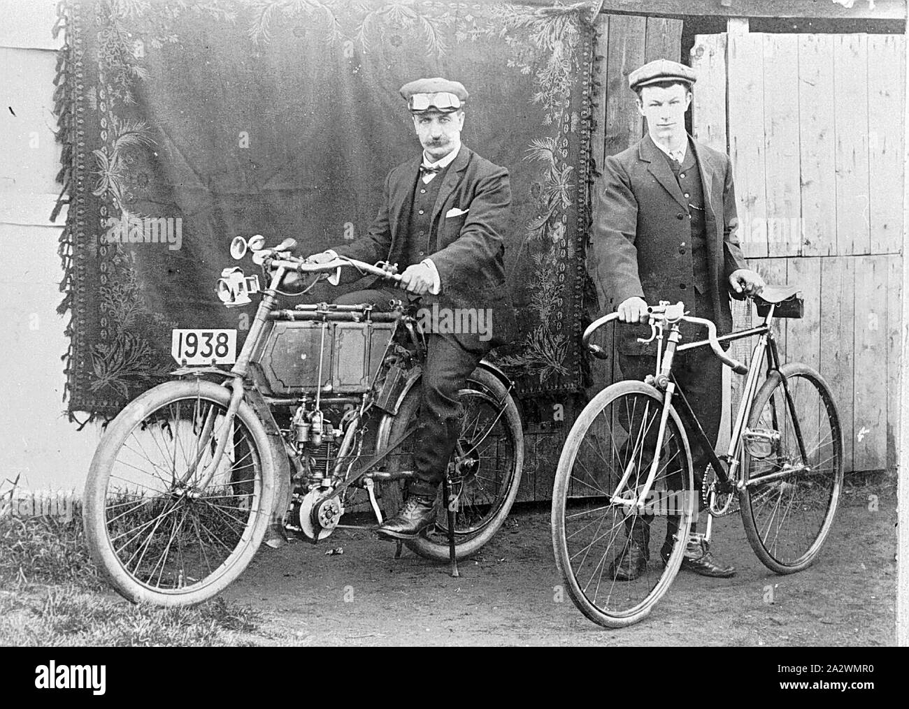 Negative - zwei Männer mit Stimulation Motorrad & Fahrrad, Canterbury, Victoria, ca. 1920, zwei Männer, eine auf einem Motorrad sitzt, der andere mit einem Fahrrad. Eine Wolldecke hat über einen Zaun im Hintergrund als Kulisse für das Foto hing Stockfoto