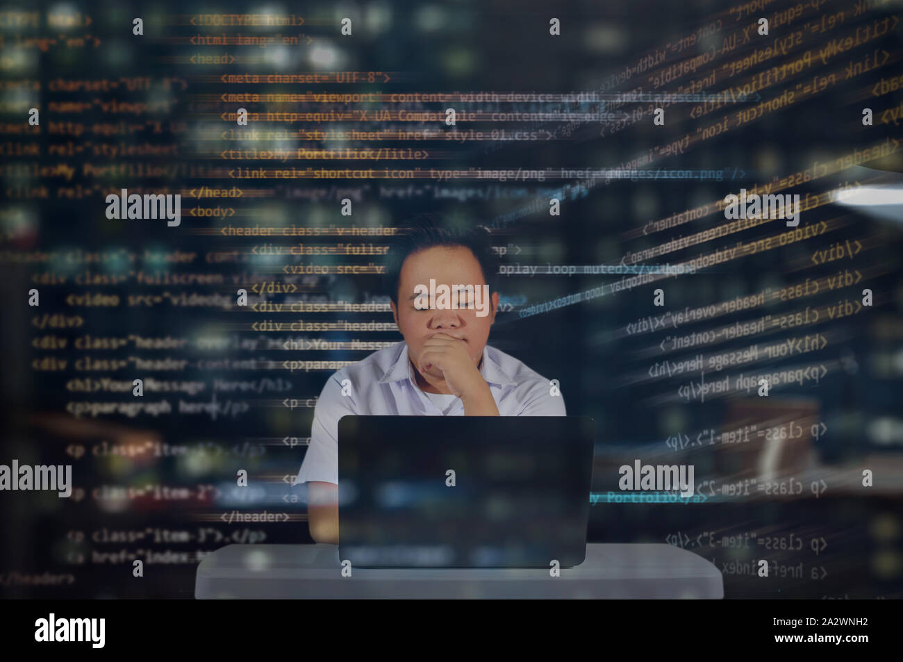 Junge es männliche Kursteilnehmer lesen seiner HTML-Codes auf einem virtuellen Hologramm Bildschirm mit seinem Laptop auf dem Schreibtisch projiziert. Denken und konzentriert arbeiten bei Nacht Stockfoto