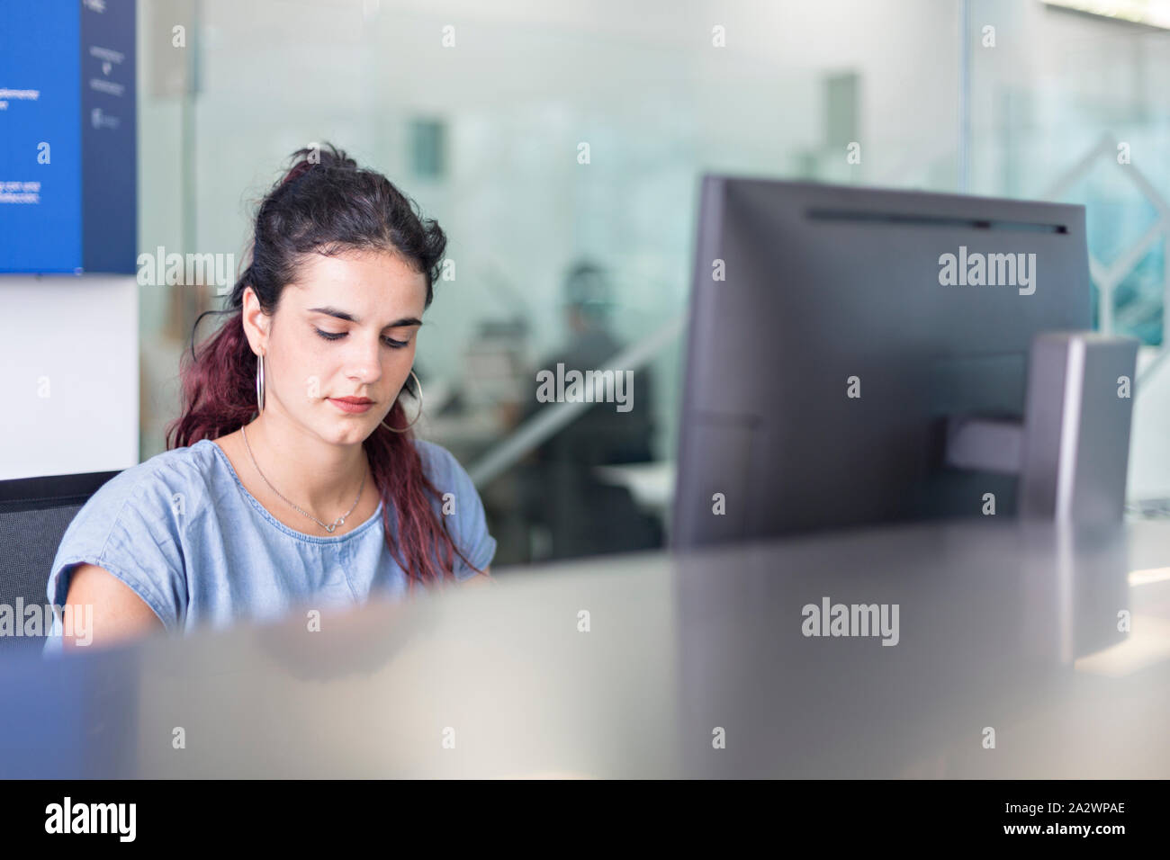 Junge Frau gerade Nachrichten auf dem Bildschirm in einem Coworking Space. Moderne Einrichtung mit Glas Divisionen für freiberufliche Mitarbeiter. Stockfoto