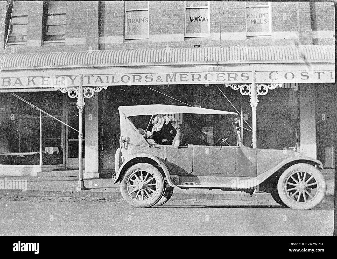 Negative - Victoria, ca. 1925, ein Auto in der Straße, eine Bäckerei und ein Schneider und Mercer. Es ist ein Kind in der Rückseite sitzt und eine Frau über ihre schiefen Stockfoto