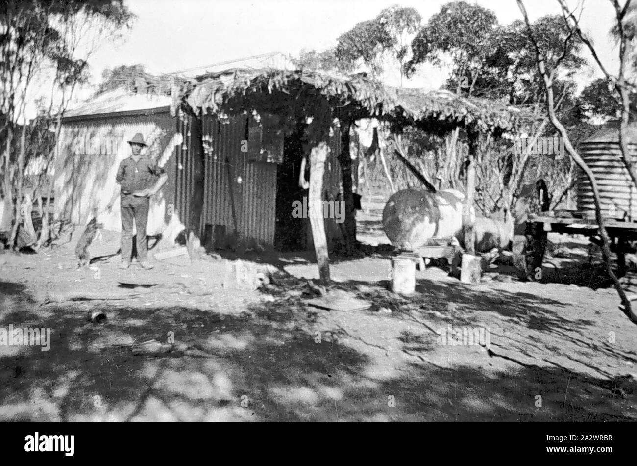Negative - Prooinga, Victoria, ca. 1925, ein Mann vor einer Hütte aus Wellblech und mit einem reetgedeckten Veranda. Es ist ein Kraftstoff (?) Tank unter der Veranda und einem Wassertank auf der rechten Seite Stockfoto