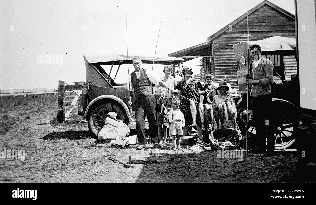Negative - Pinjarra Bezirk, Victoria, ca. 1925, eine Familie mit ihrem Fang von Fischen. Es gibt zwei Autos hinter Ihnen und ein Holzhaus im Hintergrund Stockfoto