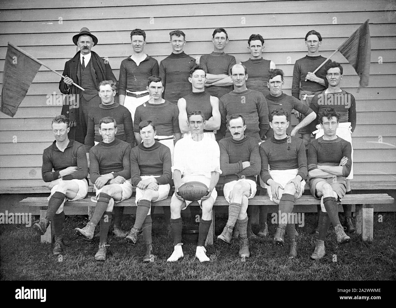 Negative - Pinjarra, Victoria, circa 1925, die traralgon Fußballmannschaft. Der Schiedsrichter sitzt in der Mitte mit dem Ball und zwei Männer Holding flags Flanke das Team Stockfoto