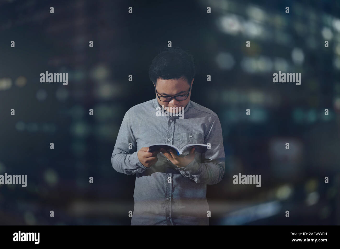 Männliche Student trägt lange Ärmel und Brillen in der Nacht ein Buch lesen friedlich innerhalb einer isolierten dunklen Zimmer. In der breiten Ansicht gedreht. Stockfoto