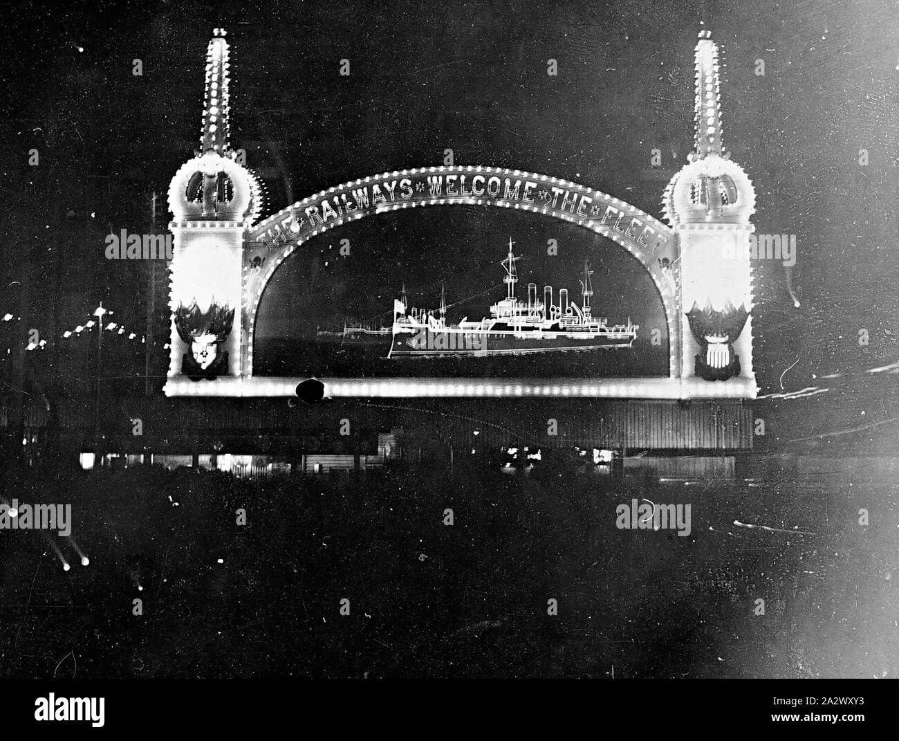 Negative - "Die Bahn begrüßt die Flotte" beleuchteten Zeichen, Melbourne, Victoria, 1913, eine beleuchtete arch Framing eine beleuchtete Schlachtschiff. Der Bogen trägt die Aufschrift "Die Bahn begrüßt die Flotte'. Die US-Marine war der Besuch in Melbourne Stockfoto