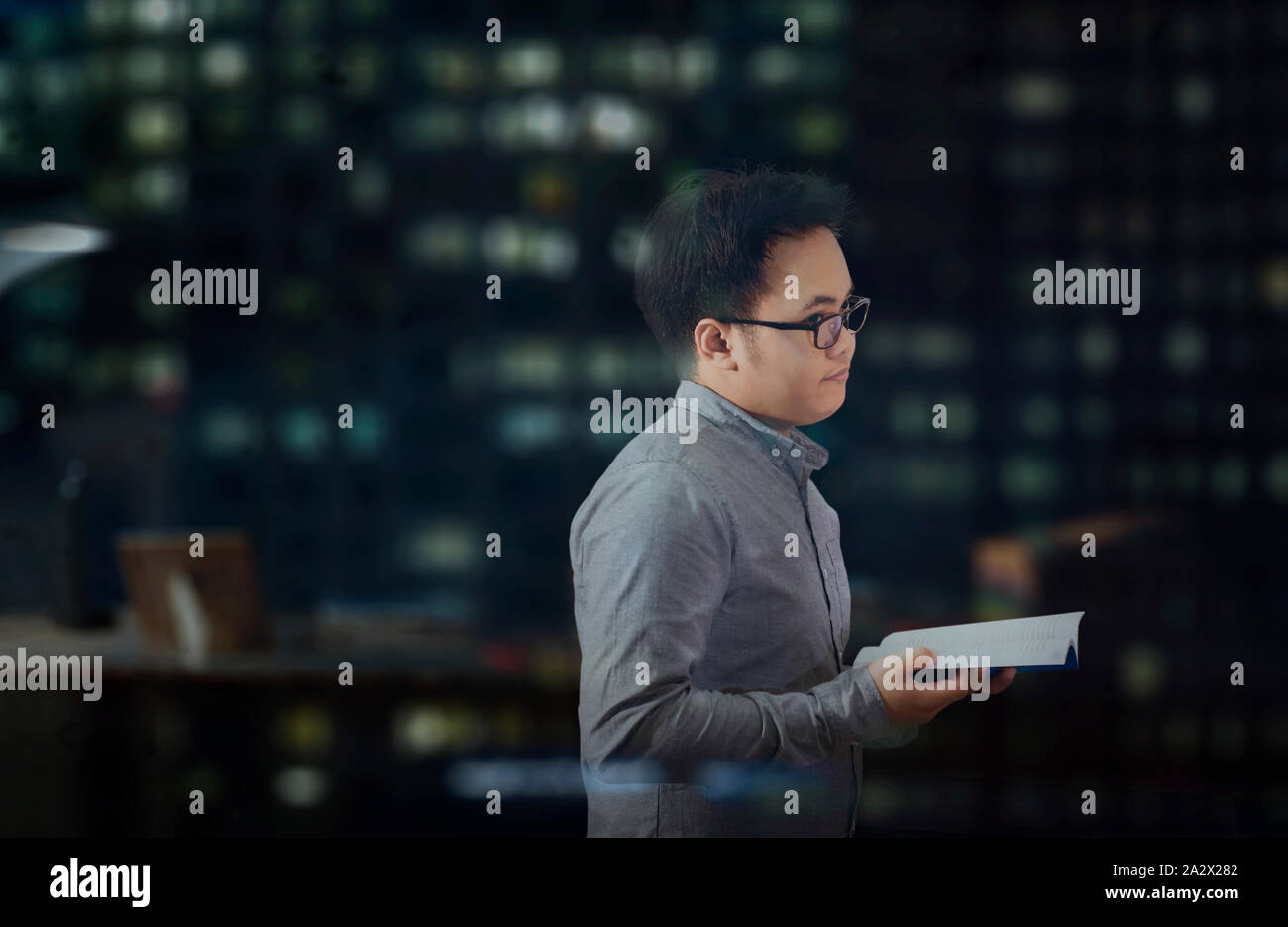 Junger Mann mit langen Ärmeln und Brillen vorübergehend an etwas anderes abgelenkt und Gedanken über etwas, während ein Buch zu lesen. Stockfoto