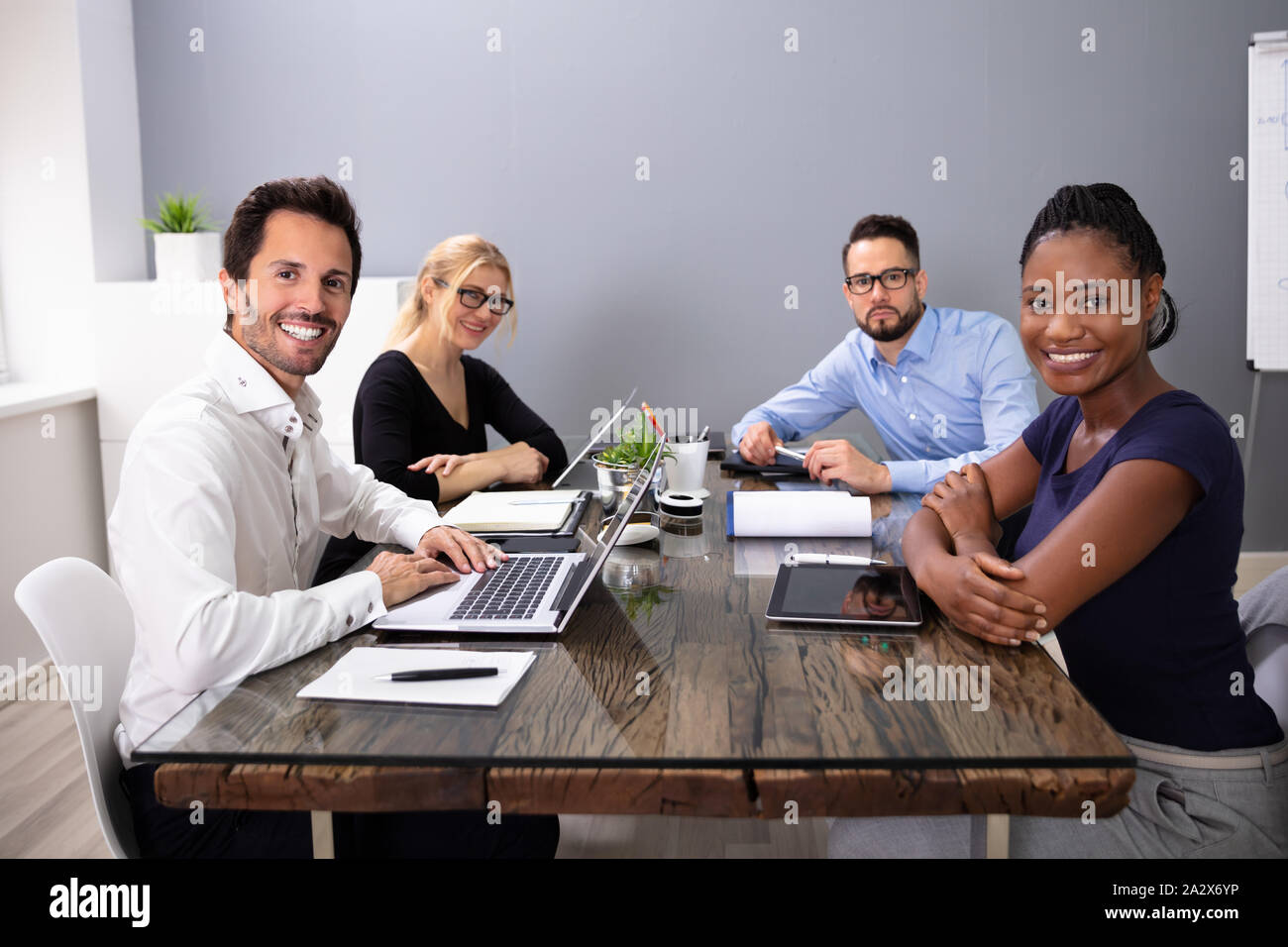 Gruppe von lächelnden Business Leute, die an der Kamera sitzt mit Laptop im Büro Stockfoto