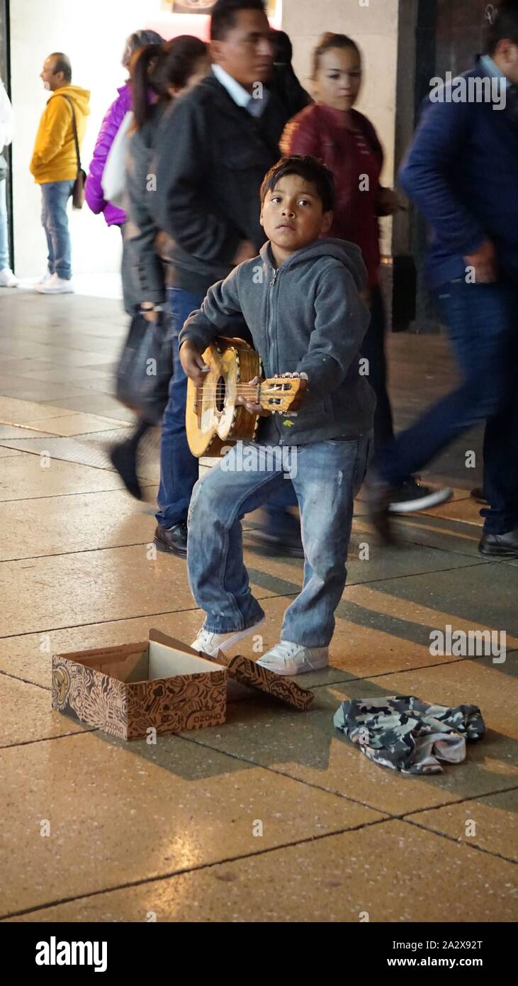 Junge spielt Gitarre auf der Straße für Geld mit Fußgänger hinter ihm an der Ave 5 de Mayo, Centro Historico, Mexico City, Mexiko Stockfoto
