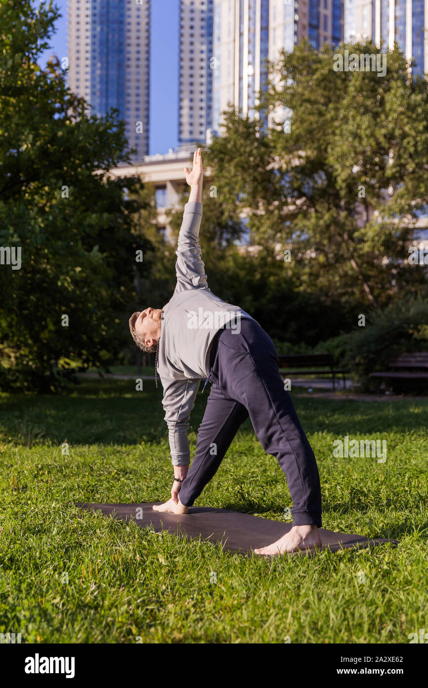 Man Yoga Asanas im City Park inspiriert. Fitness im Freien und Life Balance Konzept. Stretching. Dreieck Pose oder Trikonasana Stockfoto