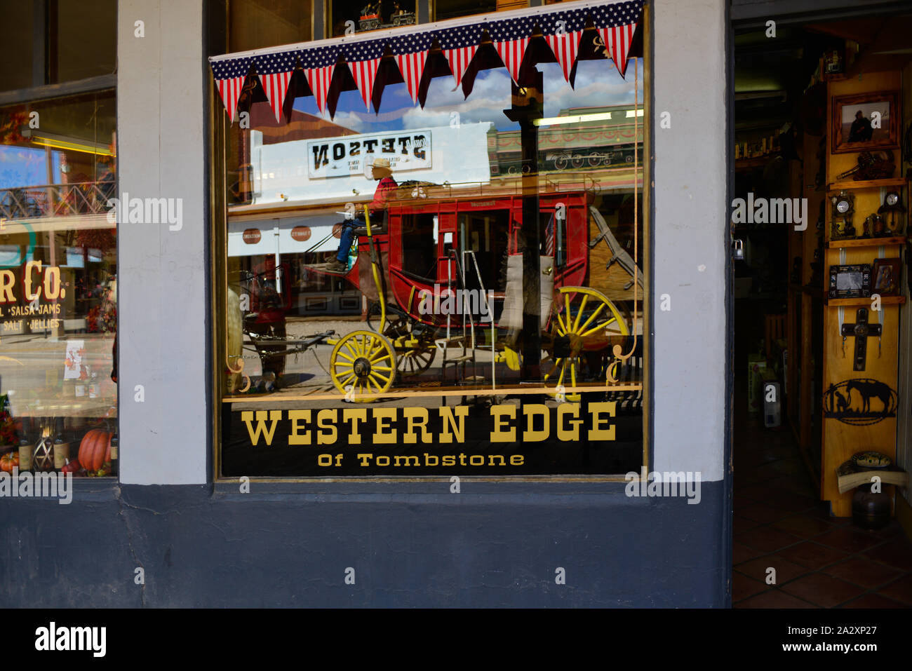 Die westliche Flanke von Tombstone Modell Bahn & Geschenke Shop, hat eine Reflexion in der Storefront Fenster eines roten Postkutsche fahren durch in Tombstone, AZ, USA Stockfoto