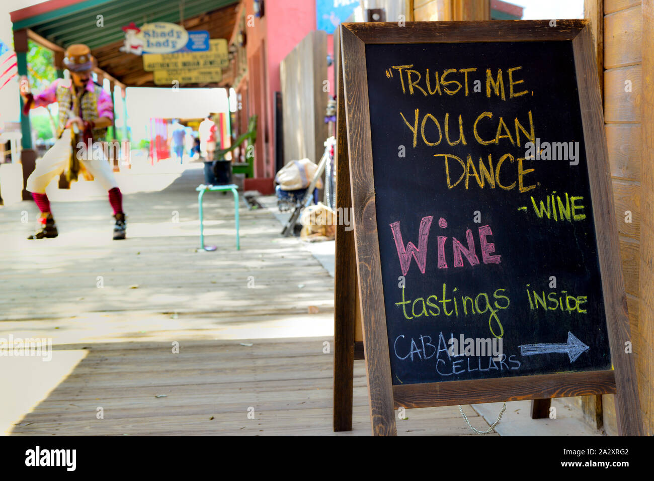 Sandwich board anmelden Förderung Weinhandlung hat lustige Zitat während Straße tanzen Interpret in der Nähe auf dem hölzernen Bürgersteigen der legendäre Tombstone, AZ, Stockfoto