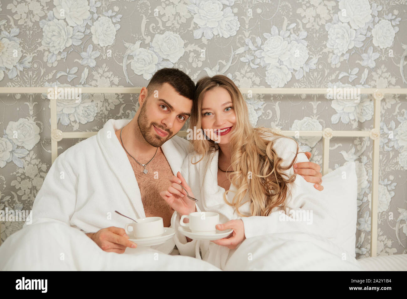Porträt eines jungen Paares in weißen Kitteln trinken Kaffee im Bett. Stockfoto