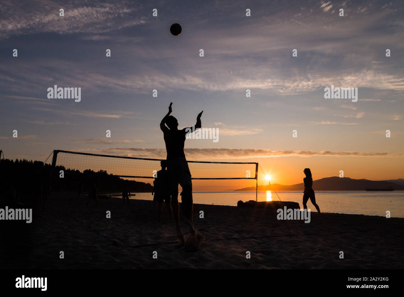 Eine Gruppe junger Leute, die Beachvolleyball spielten, spielten gegen den Sonnenuntergang am Kits Beach in Vancouver, BC. Stockfoto