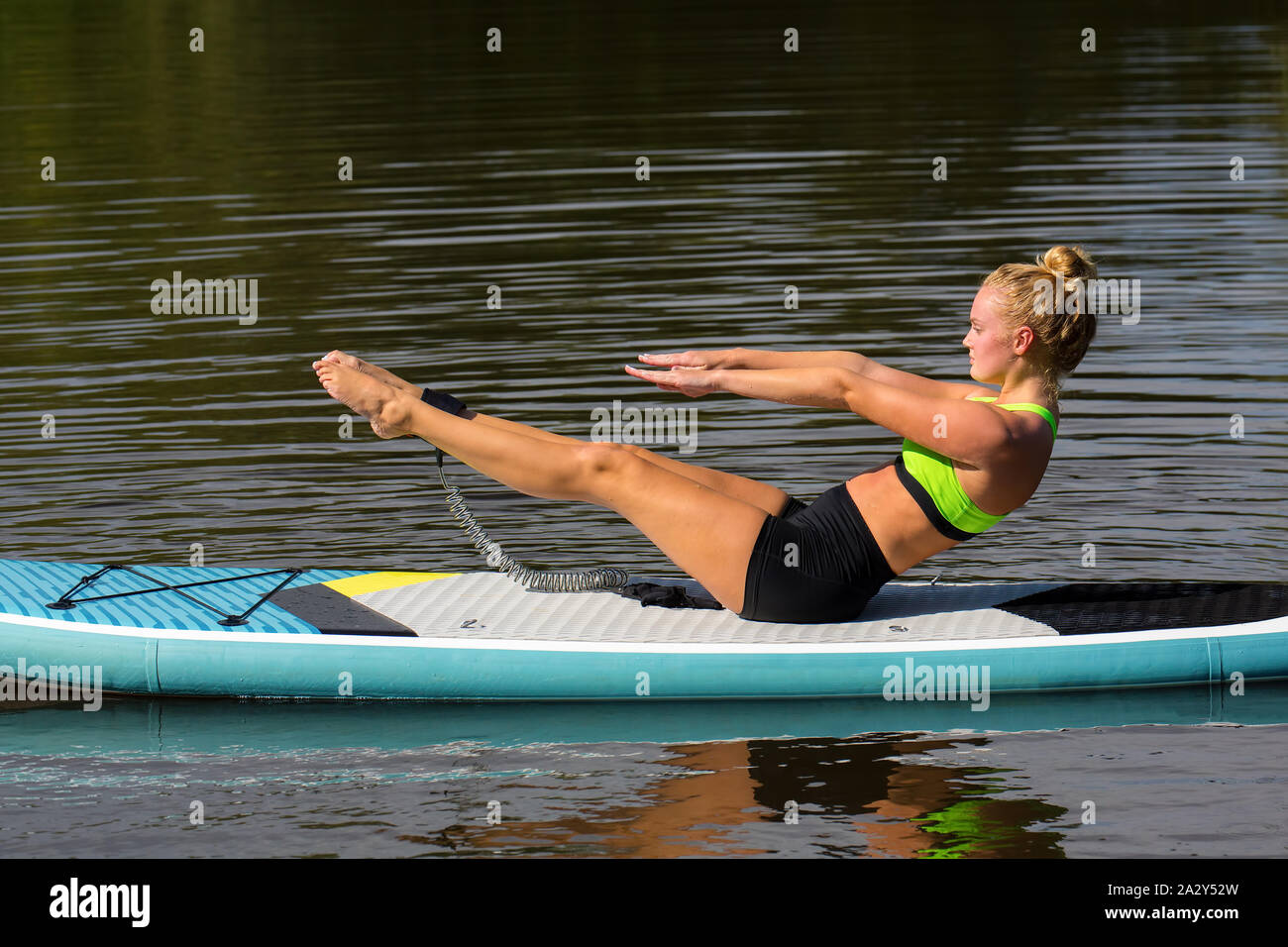 Junge Frau in Yoga Haltung auf dem Zusatzsteuerventil-armaturenbrett auf der Wasseroberfläche Stockfoto