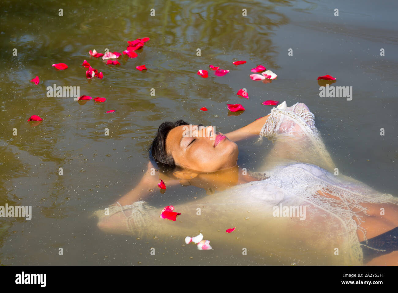 Kolumbianische Frau floating Im natürlichen Wasser mit Rosenblättern Stockfoto