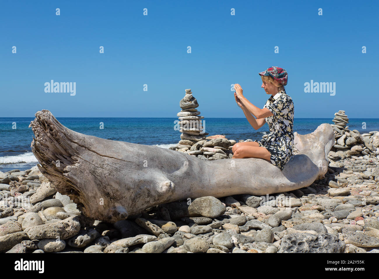 Kaukasische Frau sitzt auf Baumstamm fotografieren an der Küste Stockfoto
