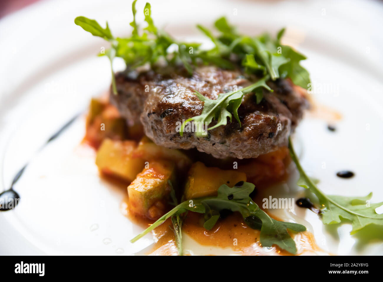 Fleisch Schnitzel mit orange Stücke von geschmortem Kürbis mit Soße und grünen Rucola Blätter eingerichtet Stockfoto