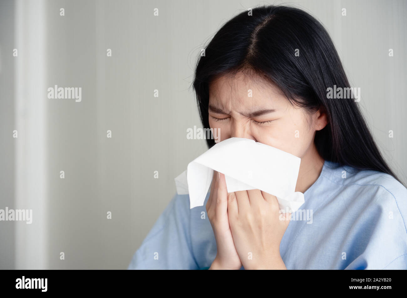 Eine junge Frau das Tragen von Kleidung des Patienten ist, Krankheit und hat Rotze. Sie nutzt das Niesen Gewebe wegen dem kalten Wetter, Sie convalesces Grippe zu Hause. Stockfoto