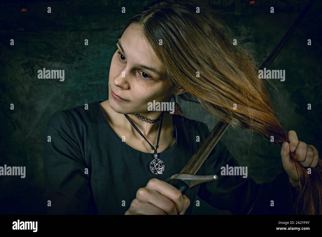 Porträt der jungen langhaarigen Frau in ein mittelalterliches Kostüm. Ständige pose mit einem Schwert an ihren Haaren an dunklen Studio Hintergrund Stockfoto