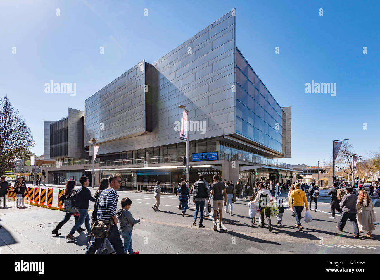 Eine große Gruppe von Menschen Überqueren einer Straße in Richtung Bahnhofshalle (Kulturzentrum) Gebäude in der Sydney Vorort von Chatswood in Australien Stockfoto
