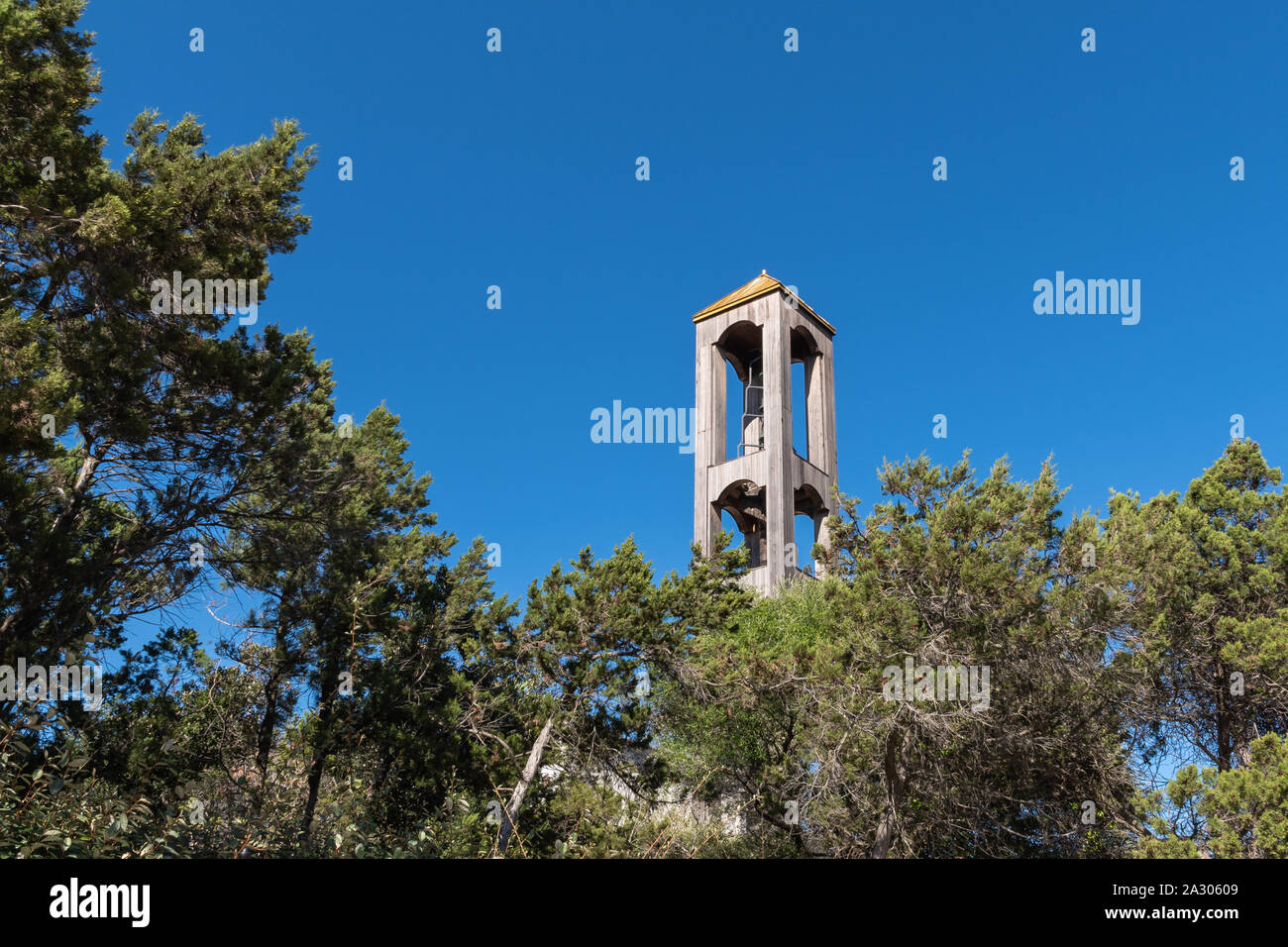 Hölzerne Glockenturm durch Äste vor blauem Himmel gerahmt Stockfoto