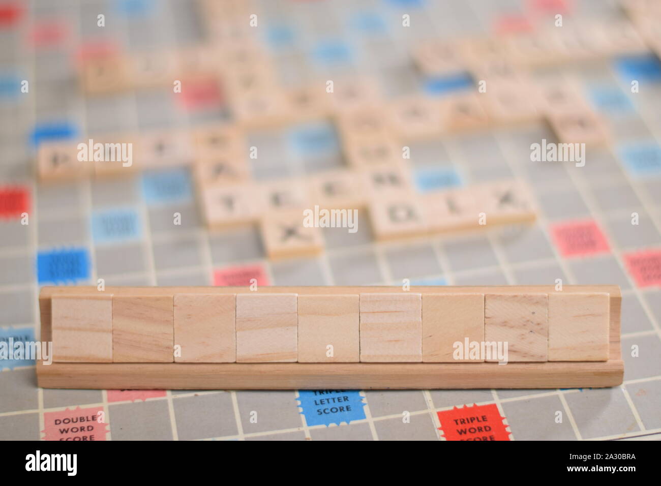 9 leere Holz- scrabble Tiles auf eine Kachel-Rack, für die Sie in Ihrem eigenen Wort zu füllen. Im Hintergrund ein Vintage board, unscharf, mit Kopie Raum Stockfoto