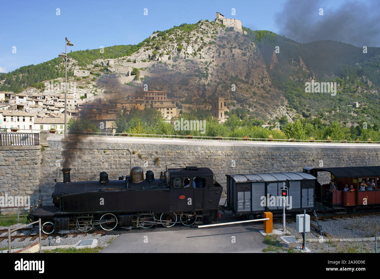 LUFTAUFNAHME von einem 6-Meter-Mast. Historischer Dampfzug, der den Bahnhof Entrevaux mit der Stadtbefestigung an der Klippe verlässt. Entrevaux, Frankreich. Stockfoto