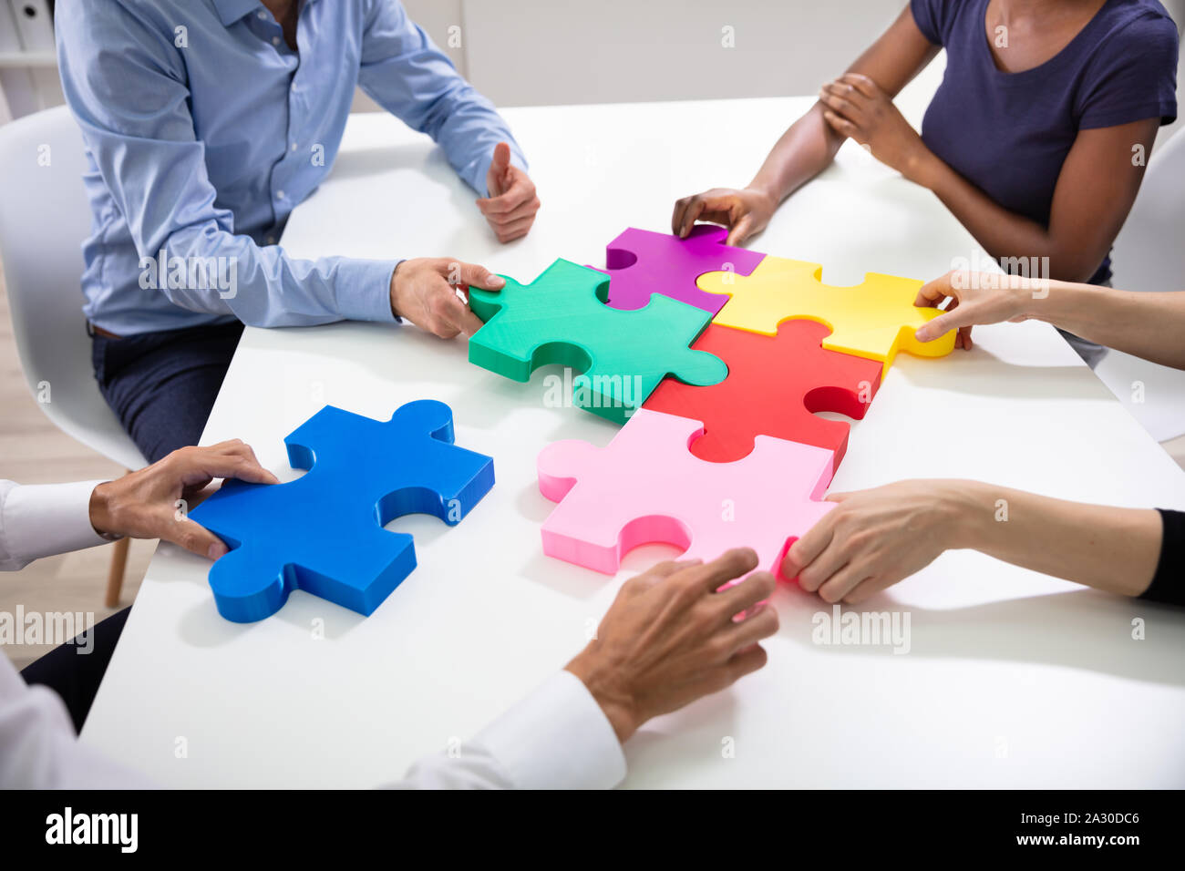 Hände von Geschäftsleuten Gebäude bunte Stichsäge Puzzles zusammen über Weiß Schreibtisch am Arbeitsplatz Stockfoto